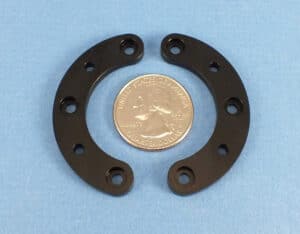 A black thin plastic machined parts with a small coin placed beside it for size comparison